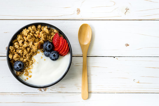 bowl of granola with yogurt, fresh berries, strawberry on wood table.