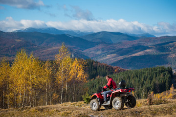Landscape of mountains, forest and blue sky with man on red quad bike at autumn sunny day. The concept of an active holiday in the mountains