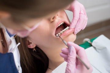 Female dentist checking up patient teeth with metal brackets at dental clinic office. Medicine,...