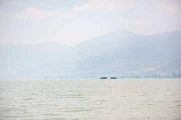 Small boat on a lake in the haze with mountains in the background, Xichang, China