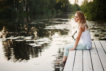 A girl sitting on a jetty and looking at a lake