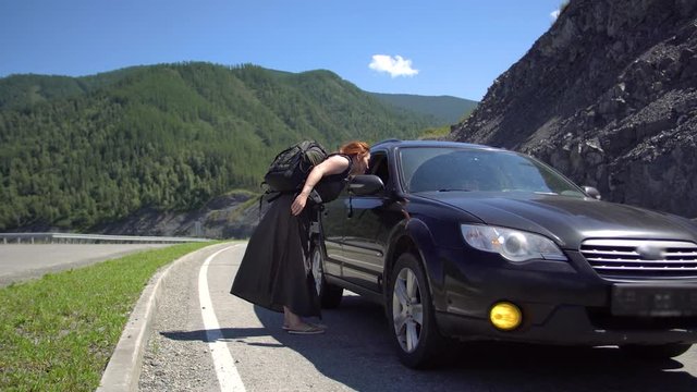 A tourist girl hitchhiking a car on a mountain road and sits down in it 4k.