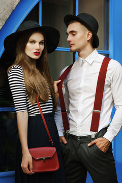 Outdoor portrait of young beautiful fashionable couple. Man and woman posing in street. Models wearing stylish clothes and accessories, elegant outfits. City lifestyle. Fashion concept