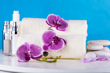 Spa. White towels, stones and orchids lie on the table, against the blue sky.