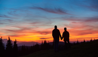 Fototapeta na wymiar Silhouettes of a man and woman tourists standing on top of a mountain stunning sunset on the background people lifestyle vitality sporty active travelling nature landscape sky.