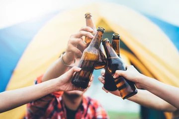 Foto op Plexiglas Friends clinking bottle of beer during camping outdoor with barbecue in background © interstid