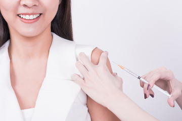 Close up hand using syringe to make vaccine injection to smile Asian female patient