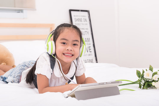 Happy Asian young girl smile while listen the music from tablet in bed.