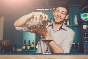 Young bartender pouring cocktail drink into glass