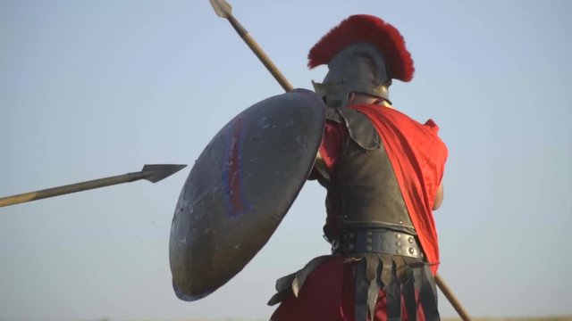 The gladiator in armor and helmet repulsed the attack with a shield and beats with a spear, slow motion
