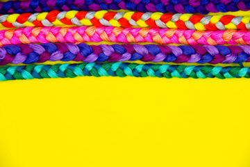 Colorful yellow background of pink, violet, yellow, green, red, purple knitted pigtail. Knitted concept. Embroidery workplace