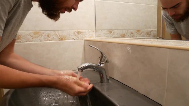 A man is washing his face with tap water.