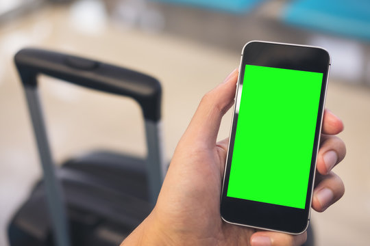 Mockup Image Of A Man's Hand Holding And Using Black Mobile Phone With Blank Green Screen With Black Baggage In Airport