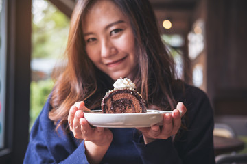 A beautiful asian woman holding chocolate cake roll and whipped cream with feeling happy and good lifestyle in the modern loft cafe