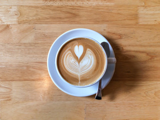 Top view of cup of hot latte coffee with latte art on wooden table in morning light. Morning coffee illustrating modern lifestyle / diet