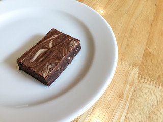 Piece of baked marble chocolate brownie on white dish on wooden table with copy space to the right, closeup shot