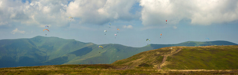 Competitions of paragliders on the ridge of Borzhava in the Carpathians in Ukraine. Panoramic photo of a large group of paragliders in the sky above the mountains.