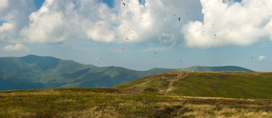 Competitions of paragliders on the ridge of Borzhava in the Carpathians in Ukraine. Panoramic photo of a large group of paragliders in the sky above the mountains.