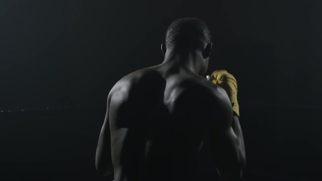 Rear view of muscular man boxing on black background. Afro american young male boxer practicing shadow boxing