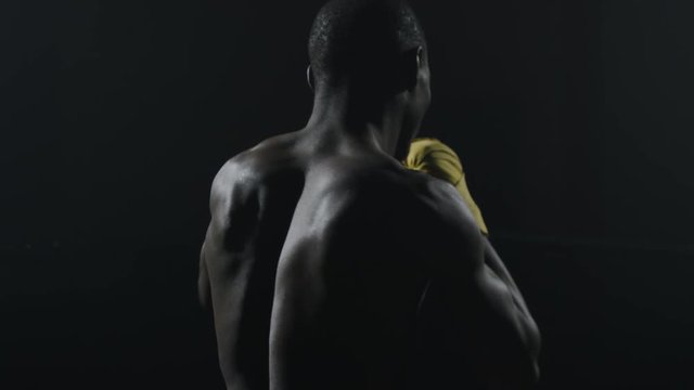 Rear view of muscular man boxing on black background. Afro american young male boxer practicing shadow boxing