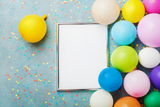 Colorful balloons, silver frame and confetti on blue table top view. Birthday or party mockup for planning. Flat lay style. Copy space for text. Festive greeting background.
