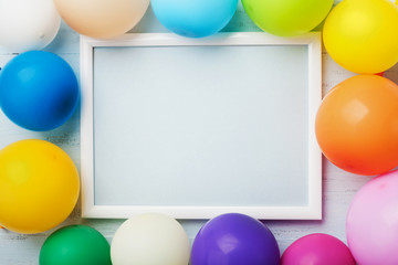 Colorful balloons and white frame on blue wooden table top view. Mockup for planning birthday or...