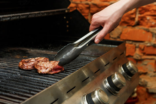 Man cooking meat steaks on professional grill outdoors