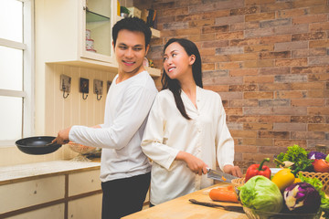 Happy asian young couple are talking and enjoying cooking food together in the lovely kitchen