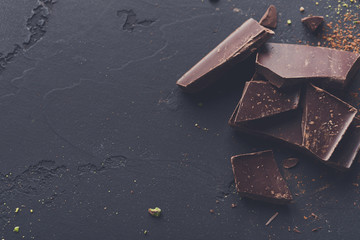Broken chocolate pieces and cocoa powder on black background