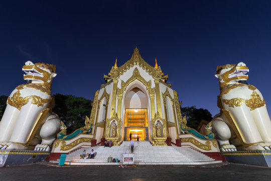 Two leogryphs guarding at the Shwedagon Pagoda's western entrance in Yangon, Myanmar at night, viewed from the front.