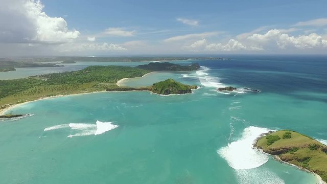 Aerial view of Tanjung Aan beach lagoon and south shores of Lombok with white sand and turquoise water surrounded by green hills. Shot with drone on sunny day with blue sky in Indonesia, fly forward.