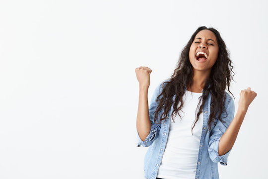 Postive human facial expressions, emotions, feelings, reaction and attitude. Attractive young Afro-american female with loose hair astonished with amazing good news, clenching fists, shouting