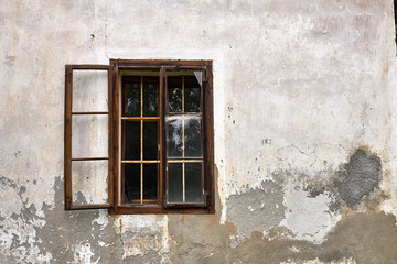 Old rotten window with rusty iron bars, with one glazing part open, in a ruined house facade