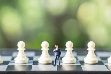 Business and work concept. Businessmen miniature mini people figures standing on chessboard with chess pieces with green nature background.