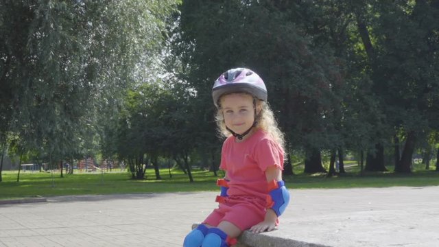 Little girl is blonde with blue eyes . Child in helmet looking at the camera,portrait of a happy girl.  Roller skating bicycle.