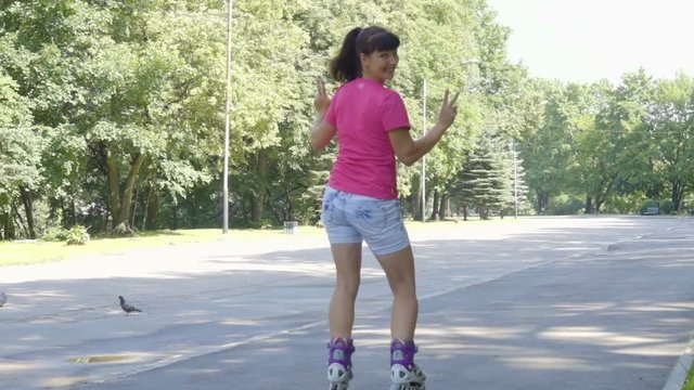 Back view of a girl in shorts on roller skates dances, whirls your ass. Beautiful girl on roller skates in skate park. Young woman goes rollerblading. Outdoor activities in summer. Roller skating.