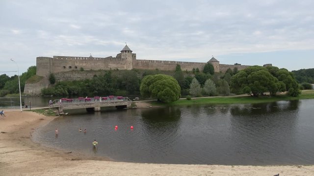 The view of the city beach at the walls of the Ivangorod fortress, cloud on a summer day