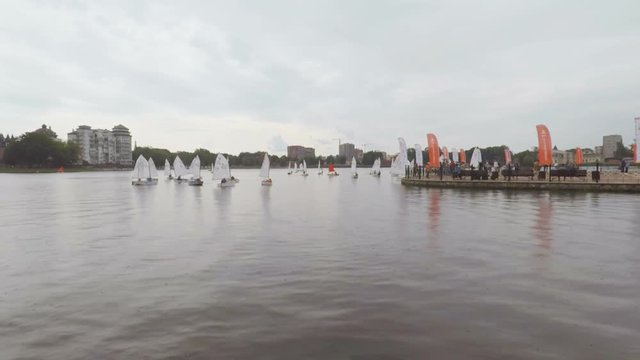 Children's sailing regatta on a rainy day. Many sailing boats, cruising in front of the audience, youth sailing regatta, sailboats competing.  Kaliningrad - July 2017 Russian.
