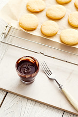 Baked butter cookies with dark chocolate drizzle glaze on a baking paper and wire rack. White wooden table. 