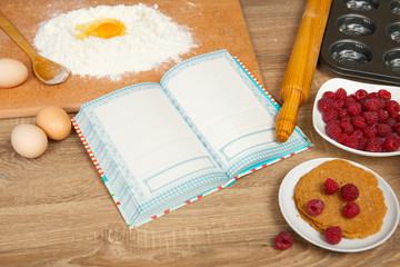 Blank cooking book and ingredients for baking cookies - flour, broken egg, cherry, strawberry on wooden background. Raw food and kitchen utensils. Healthy food concept.