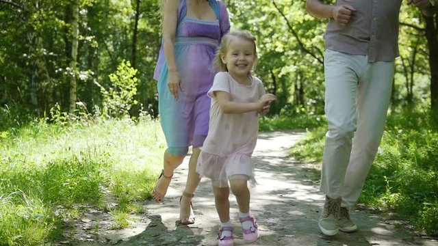 Happy family - little girl is running toward to the camera in park, slow-motion