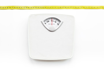 Bathroom scale and measuring tape on white background top view
