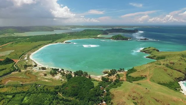 Aerial view of Tanjung Aan beach lagoon and south shores of Lombok with white sand and turquoise water surrounded by green hills. Shot with drone on sunny day with blue sky in Indonesia, fly forward.