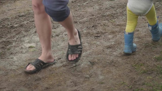 Legs of adult and toddler in rubber boots walking in mud toward one another