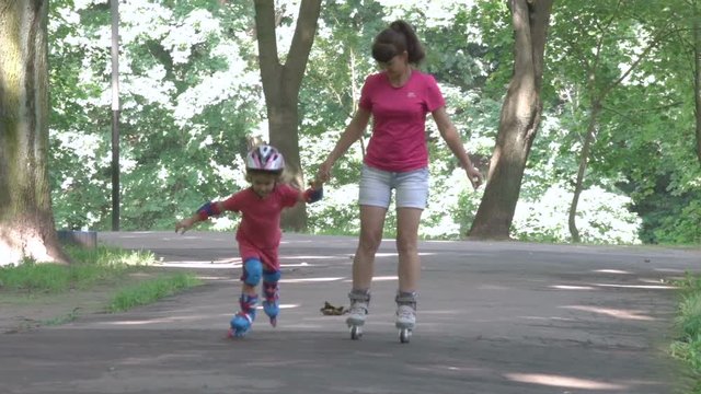  Family, young mother and daughter ride in a roller-skating park. A little girl and young woman in a helmet and defense skates on roller skates. The child rolls on the rollers in the park.  