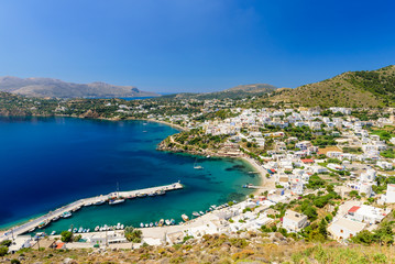 Naklejka na ściany i meble The picturesque Greek Islands. Aerial view of the coastline and the Panteli village, a traditional Greek village with white buildings and fishing boats, Leros island, Greece