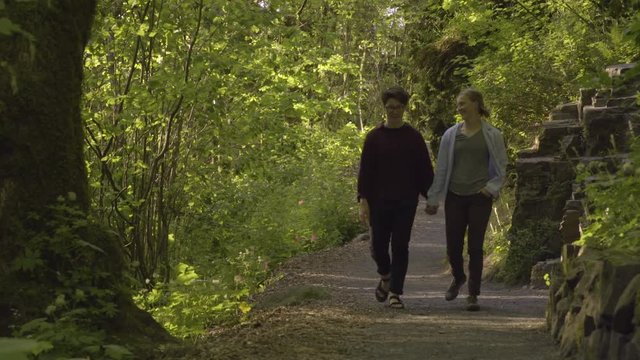 Happy Couple Holds Hands And Walks Along Hiking Trail Through Forest In Pacific Northwest