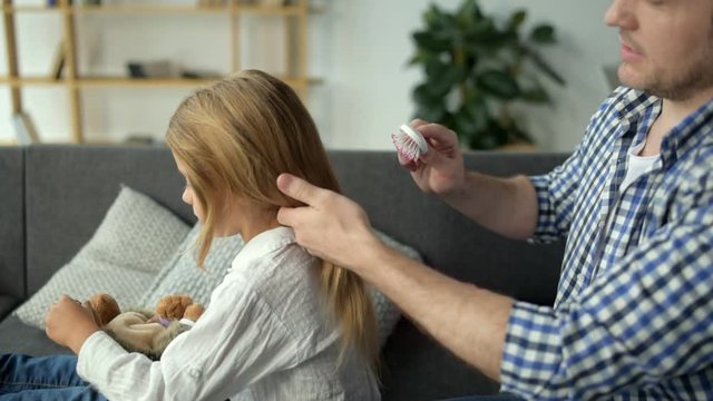 Positive father brushing hair of his nice daughter