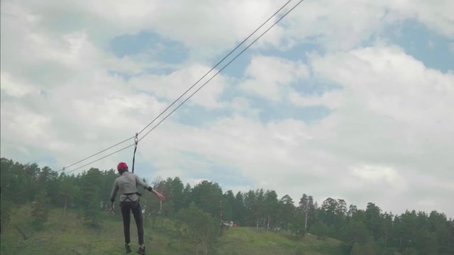 Girl in red helmet rides zip line on cloudy summer day