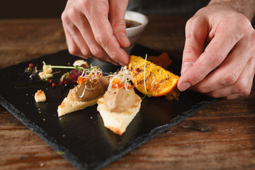 Culinary art of serving appetizers in restaurant. Small canapes with paste, decorated grilled orange and herbs on black tray